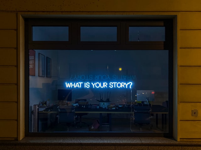 Neon in a window that says What is your Story
